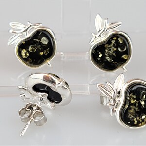 May include: A pair of silver earrings with green amber stones shaped like apples. The earrings have a delicate leaf design.