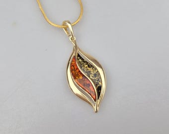 May include: A gold-toned pendant shaped like a stylized leaf, featuring two inlaid sections of amber-colored resin. One section is a warm, translucent orange, while the other is a deep, dark brown. The pendant hangs from a matching gold-toned chain.