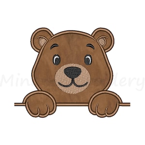 May include: A brown bear embroidery design with a smiling face, black nose, and small, round eyes. The bear's paws are holding onto a horizontal line. The design is on a white background.