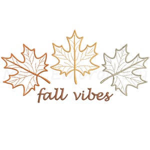May include: Three embroidered maple leaves in shades of orange, gold, and silver-gray, arranged above the phrase "fall vibes" in brown script. The design is set against a white background, evoking autumn.