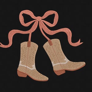 May include: Embroidered design of two cowboy boots hanging from a peach-colored bow on a black background. The boots are tan with white accents and a decorative pattern. The bow has long, flowing ribbons.