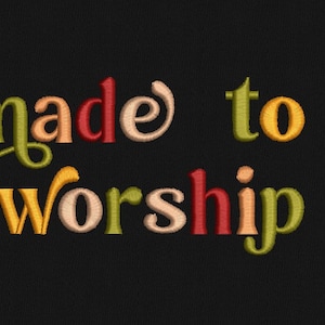 May include: Embroidered text on a black background that reads "made to worship" in colorful, stylized lettering.