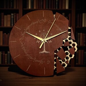 May include: A circular wooden clock in dark brown. The clock face has a tree design and script, with a section broken away to show a honeycomb pattern. The clock hands are gold. The clock would suit a study.