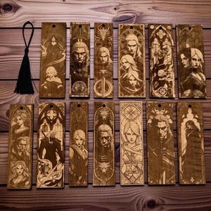 Op de afbeelding: Een verzameling houten bladwijzers met gegraveerde karakterportretten en ontwerpen. De bladwijzers tonen gedetailleerde illustraties van figuren, met een zwarte kwast aan één bevestigd. Het hout heeft een warme, natuurlijke tint.
