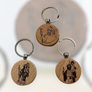 May include: Three wooden keyrings with silver key rings. Each keychain features a circular wooden charm with a black and white image of a religious figure.