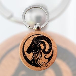 May include: A wooden keychain with a black and white engraved image of an Aries zodiac sign. The keychain is attached to a silver metal ring.