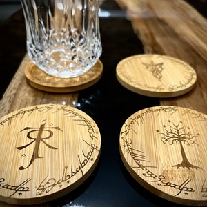 Pode incluir: Quatro  t&aacute;buas redondas de madeira com desenhos gravados do Senhor dos An&eacute;is. Uma t&aacute;bua apresenta o s&iacute;mbolo do Um Anel, outra a &Aacute;rvore Branca de Gondor, e duas t&ecirc;m a inscri&ccedil;&atilde;o "Um Anel para govern&aacute;-los a todos".