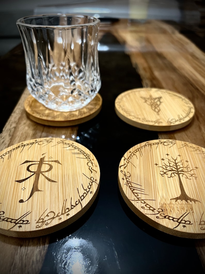 Pode incluir: Quatro  t&aacute;buas redondas de madeira com desenhos gravados do Senhor dos An&eacute;is. Uma t&aacute;bua apresenta o s&iacute;mbolo do Um Anel, outra a &Aacute;rvore Branca de Gondor, e duas t&ecirc;m a inscri&ccedil;&atilde;o "Um Anel para govern&aacute;-los a todos".