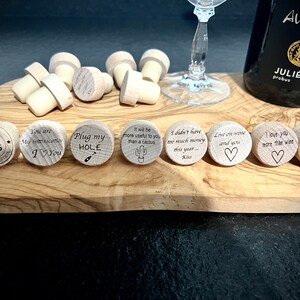 May include: A set of ten wooden bottle stoppers with various engraved messages. The messages include "You are my intoxication I love you", "Plug my hole", "It will be more useful to you than a cactus", "I didn't have too much money this year... Kiss", "Live on wine and you", "I love you more than wine", and "Toast Daddy!"