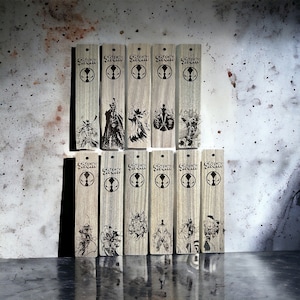 Könnte beinhalten: Ein Set mit 11 Holz-Lesezeichen mit dem Comic-Charakter Spawn. Jedes Lesezeichen ist mit dem Wort "Spawn" und einem anderen Bild des Charakters graviert.