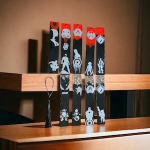Può includere: Set di sei segnalibri in resina nera e rossa con vari personaggi e loghi di supereroi. I segnalibri sono lunghi circa 15 cm e hanno un rivestimento in resina trasparente.