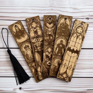 Pode incluir: Um conjunto de marcadores de livros de madeira com personagens da DC Comics, incluindo Batman e The Joker. Cada marcador tem um design único com um borla preta anexada. Os marcadores são feitos de madeira castanha clara.