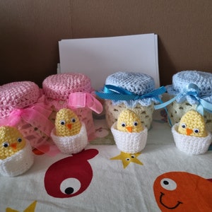 Puede incluir: Cuatro tarros de crochet con pollitos dentro. Los tarros están decorados con tapas y cintas de crochet rosa, azul y blanco. Los pollitos son amarillos con nidos de crochet blanco.