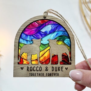 May include: Wooden ornament with a rainbow swirl design and two dog silhouettes. The ornament is personalized with the names "Rocco & Duke" and the text "Together Forever".