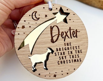 Könnte beinhalten: Ein hölzerner Weihnachtsbaumschmuck mit einem goldenen Stern und einer Ziege. Der Anhänger ist mit dem Namen "Dexter" und dem Text "Der hellste Stern am Himmel dieses Weihnachten" personalisiert.