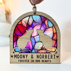 May include: Wooden ornament featuring a stained glass design in shades of pink, purple, blue, and red. Two rat silhouettes are inside the stained glass design. The ornament has the text "Moony & Norbert" and "Forever in our hearts" engraved on the bottom.