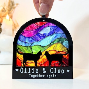 Op de afbeelding: Een zwarte acryl gedenk ornament met een regenboog glas-in-lood ontwerp en twee zwarte kat silhouetten. De tekst "Ollie & Cleo" en "Together again" is gedrukt onder de katten.