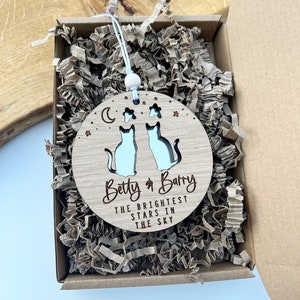 May include: A wooden ornament featuring two cats and stars, a crescent moon, and the text "Betty & Barry The Brightest Stars In The Sky".