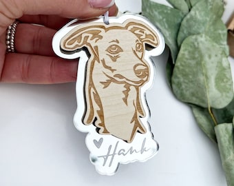 Op de afbeelding: Een zilveren spiegelornament met een lasergesneden ontwerp van een hondenkop. De naam van de hond, "Hank", is gegraveerd op het ornament.