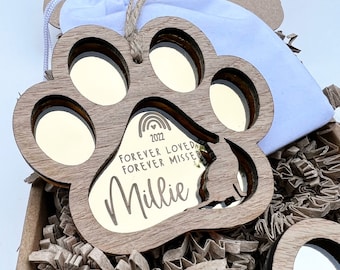 May include: A wooden paw print ornament with a mirrored surface. The ornament has a rainbow, the year 2022, and the text "Forever Loved Forever Missed" engraved on it. The name "Millie" is also engraved on the ornament.