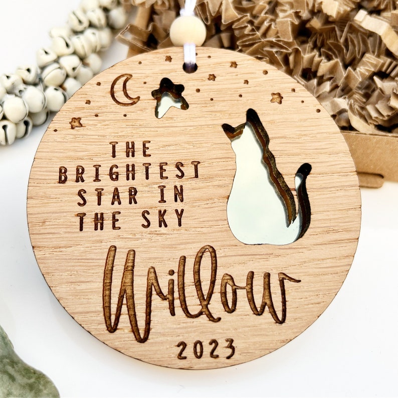 May include: A wooden ornament with a cat silhouette, a crescent moon, and a star. The text reads "The brightest star in the sky Willow 2023".