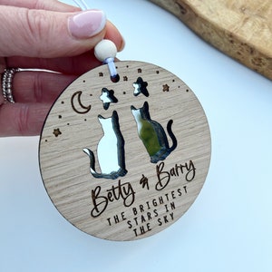 May include: Wooden ornament featuring two cats gazing at each other, a crescent moon, and stars. The ornament is engraved with the text "Betty & Barry The Brightest Stars In The Sky".
