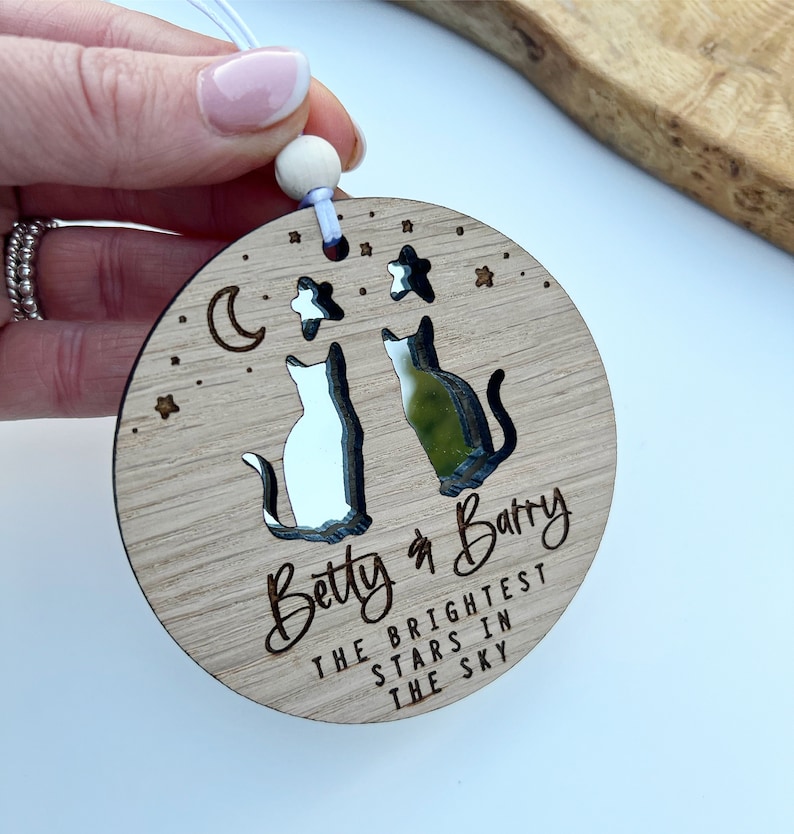 May include: Wooden ornament featuring two cats gazing at each other, a crescent moon, and stars. The ornament is engraved with the text "Betty & Barry The Brightest Stars In The Sky".