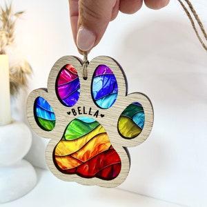 Peut inclure: Ornement en bois en forme de patte d'animal avec un motif en spirale arc-en-ciel et le nom "BELLA" au centre.