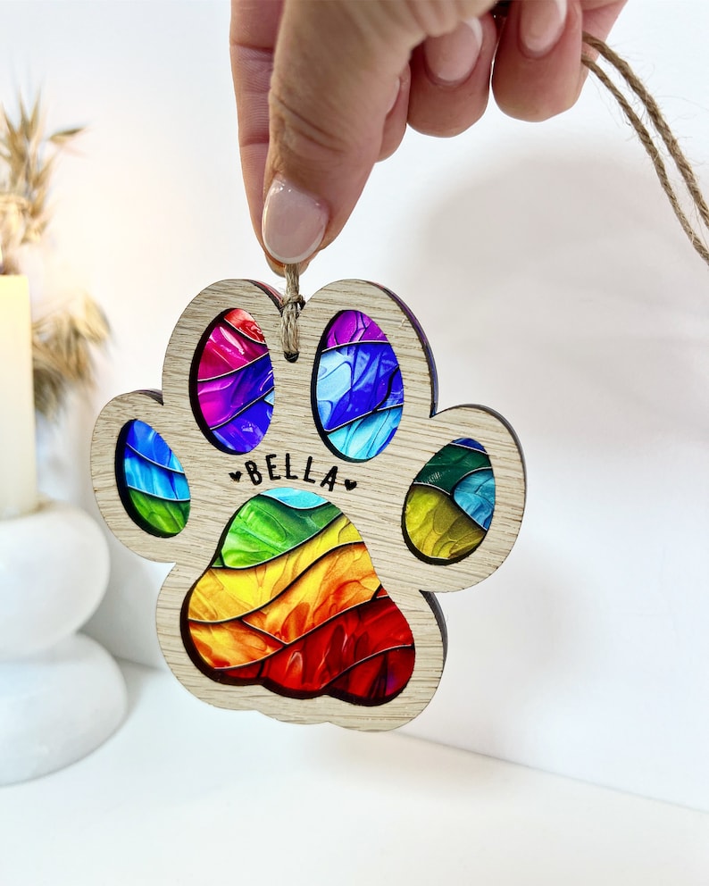 Peut inclure: Ornement en bois en forme de patte d'animal avec un motif en spirale arc-en-ciel et le nom "BELLA" au centre.