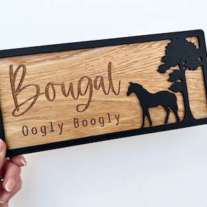 May include: A wooden sign with a black frame and a horse silhouette. The sign says "Bougalt Oogly Boogly" in a cursive font.