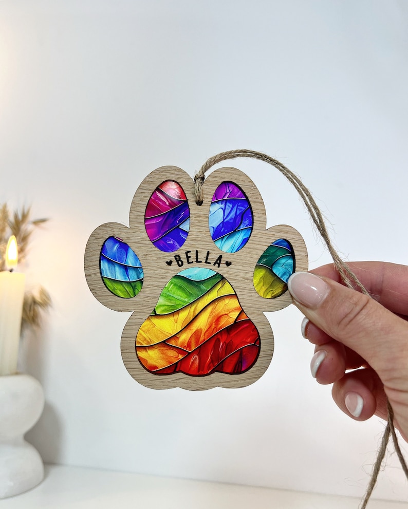 Peut inclure: Une d&eacute;coration de No&euml;l en bois en forme de patte d'animal avec un motif en spirale arc-en-ciel et le nom "BELLA" inscrit dessus. La d&eacute;coration est attach&eacute;e &agrave; une ficelle en ficelle.