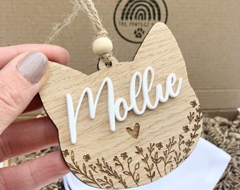 May include: A wooden cat-shaped ornament with the name "Mollie" engraved in white lettering. The ornament is decorated with a small heart and a floral design.