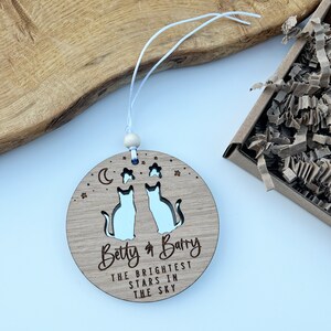 May include: A wooden ornament featuring two cut-out cats, a crescent moon, and stars. The ornament is inscribed with "Betty & Barry The Brightest Stars In The Sky".