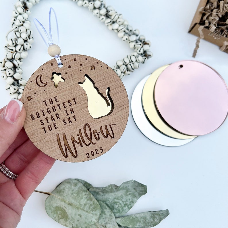 May include: A wooden ornament with a cat silhouette, stars, and a crescent moon. The text reads "The brightest star in the sky Willow 2023".