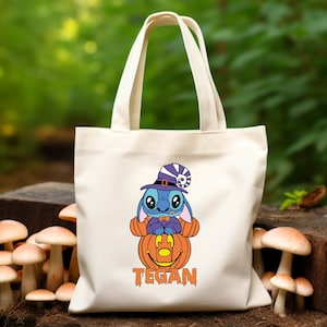May include: White canvas tote bag with a blue Stitch character wearing a witch hat and holding a jack-o'-lantern. The bag has the name "TEGAN" printed on the bottom.