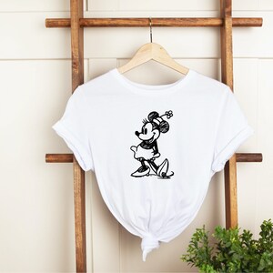 Pu&ograve; includere: Maglietta bianca con uno schizzo in bianco e nero di Minnie Mouse con un fiocco e un fiore.