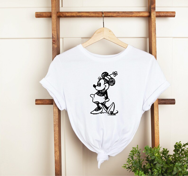 Pu&ograve; includere: Maglietta bianca con uno schizzo in bianco e nero di Minnie Mouse con un fiocco e un fiore.