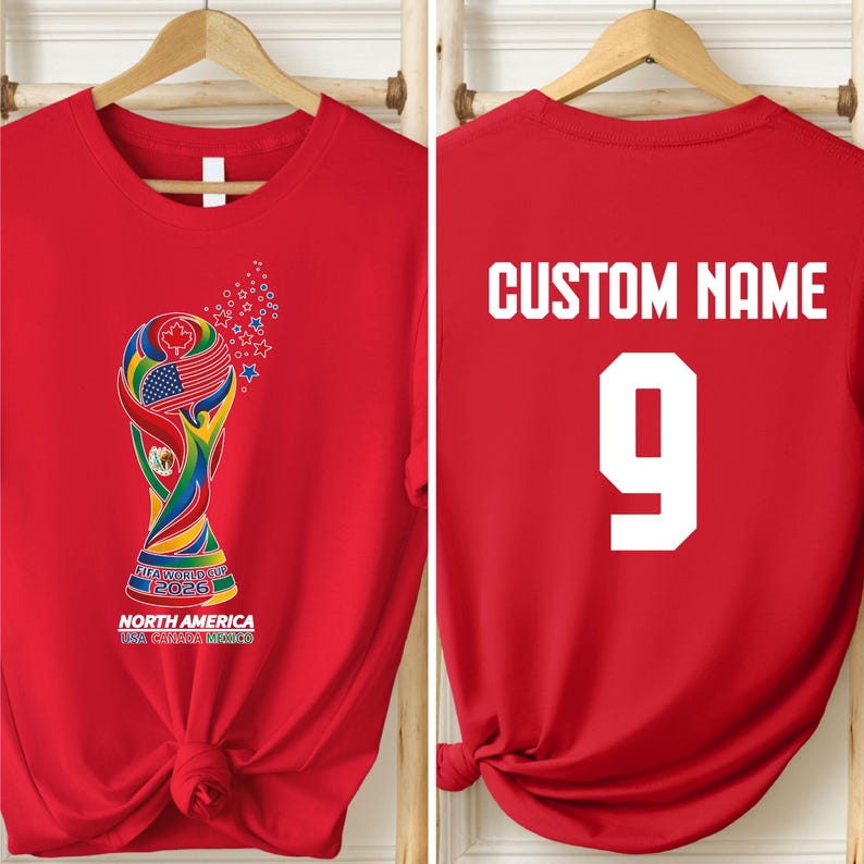A red t-shirt with a colorful graphic of the FIFA World Cup trophy and the text "NORTH AMERICA USA CANADA MEXICO" printed on it. The t-shirt also has the text "CUSTOM NAME" and the number "9" printed on the back.