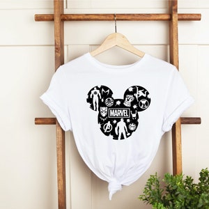 May include: White t-shirt with a black Mickey Mouse silhouette design featuring various Marvel characters, including Iron Man, Captain America, Thor, Black Panther, and more. The word "MARVEL" is printed in the center of the design.