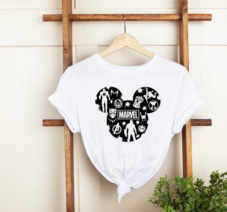 May include: White t-shirt with a black Mickey Mouse silhouette design featuring various Marvel characters, including Iron Man, Captain America, Thor, Black Panther, and more. The word "MARVEL" is printed in the center of the design.