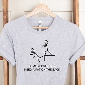Peut inclure: T-shirt gris avec une illustration de personnages en bâtonnets, l'un donnant une tape dans le dos à l'autre. Le texte dit "Some people just need a pat on the back."