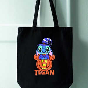 May include: Black tote bag with a blue Stitch character wearing a witch hat and sitting on a jack-o'-lantern. The bag has the name "TEGAN" printed on the bottom.
