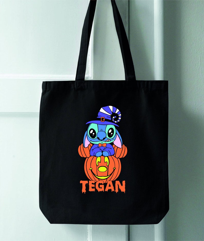 May include: Black tote bag with a blue Stitch character wearing a witch hat and sitting on a jack-o'-lantern. The bag has the name "TEGAN" printed on the bottom.