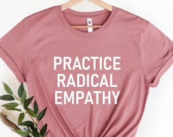 Może przedstawiać: Różowy t-shirt w kolorze pudrowego różu z nadrukiem "PRACTICE RADICAL EMPATHY" w kolorze białym.