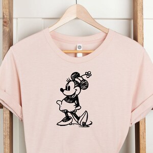 Pu&ograve; includere: Una maglietta rosa con uno schizzo in bianco e nero di Minnie Mouse sul davanti.