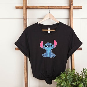 May include: Black t-shirt with a blue Stitch character from Lilo & Stitch. Stitch is sitting with his arms crossed and has pink ears.