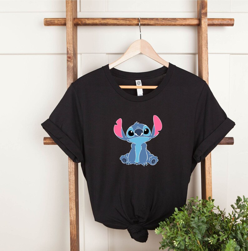 May include: Black t-shirt with a blue Stitch character from Lilo & Stitch. Stitch is sitting with his arms crossed and has pink ears.