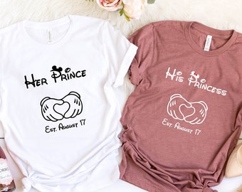 Op de afbeelding: Twee T-shirts met een Mickey Mouse handhartontwerp. Het witte T-shirt zegt "Her Prince" en het kastanjebruine T-shirt zegt "His Princess". Beide shirts hebben de tekst "Est. August 17".
