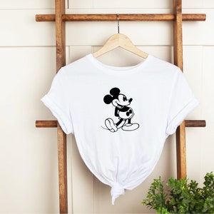 May include: White t-shirt with a black and white image of Mickey Mouse. Mickey Mouse is smiling and has his arms crossed.