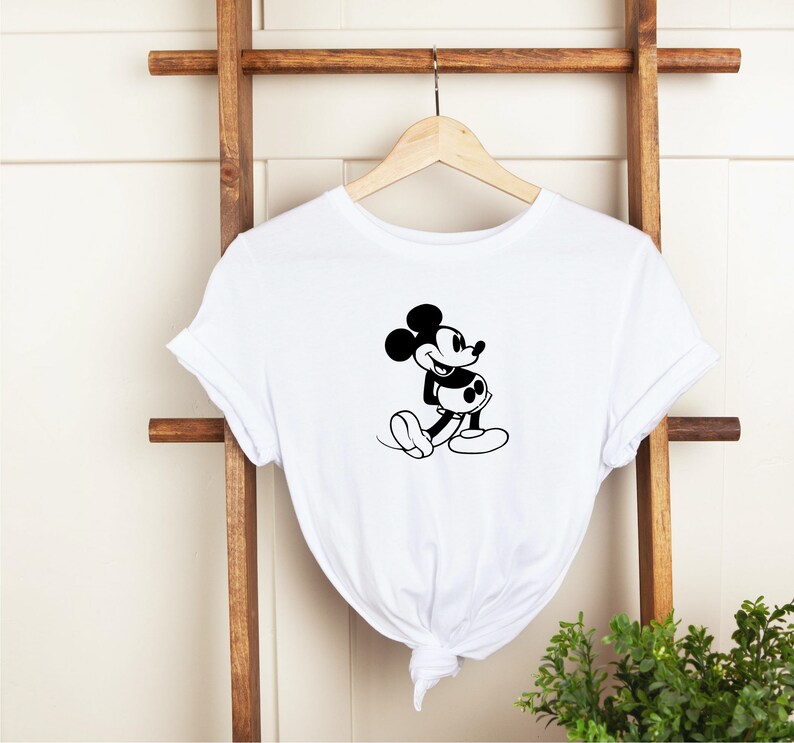 May include: White t-shirt with a black and white image of Mickey Mouse. Mickey Mouse is smiling and has his arms crossed.
